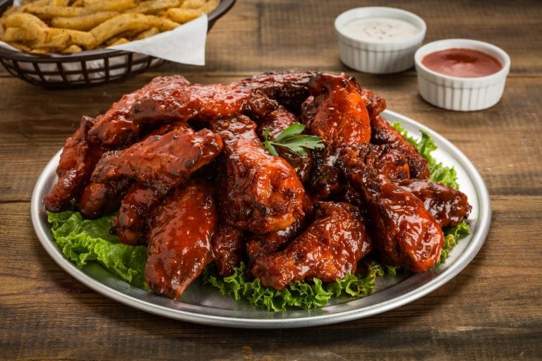 Crispy barbecue chicken wings glazed with BBQ sauce, served with creamy ranch dipping sauce on a white plate